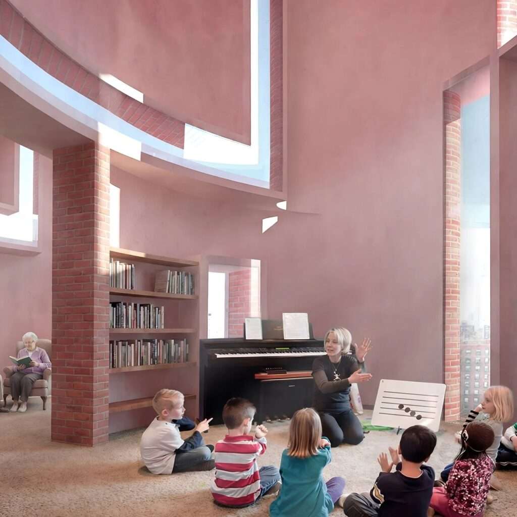 Interior classroom with curved pink walls and brick pillars where a music teacher instructs young children on the floor, while an elderly resident reads in the background.