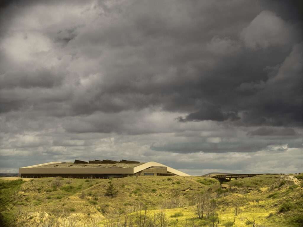 The library building seen from above under a dramatic cloudy sky, showing its low-profile integration with the hilly terrain.