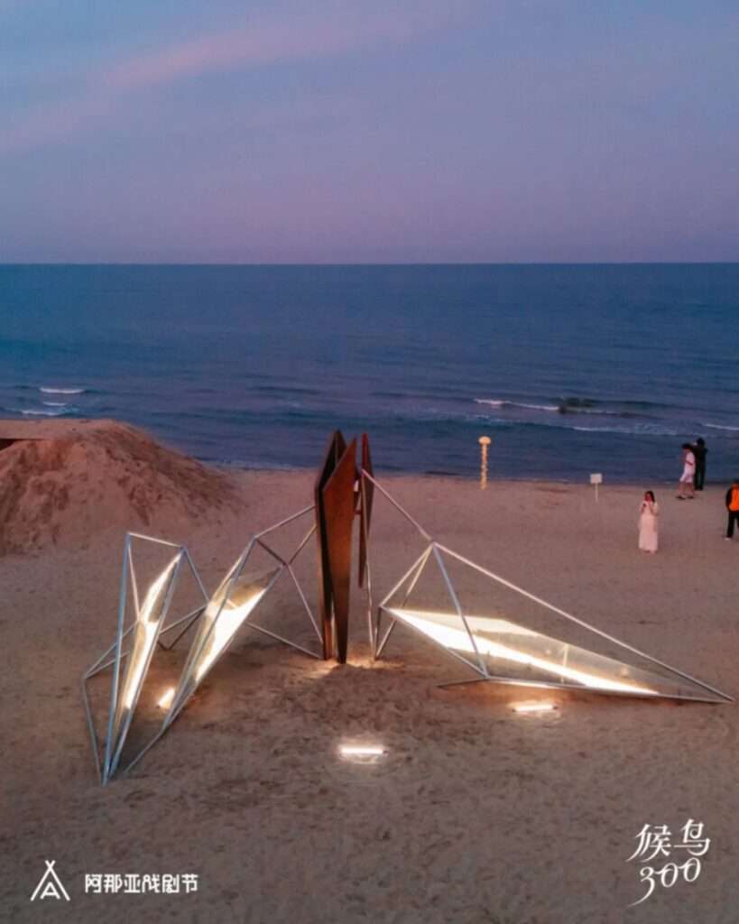 Elevated dusk view of the illuminated pavilion on the beach with glowing acrylic boxes floating in the structure.