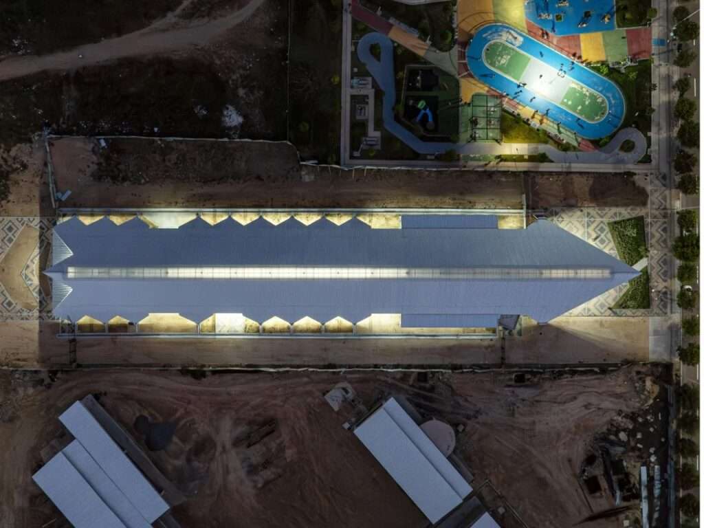 Nighttime top-down aerial photograph of the long cultural center roof glowing with perimeter lighting.
