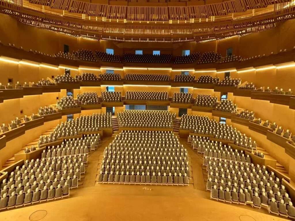 Wide interior view of a golden-hued, tiered opera house auditorium with empty seats.