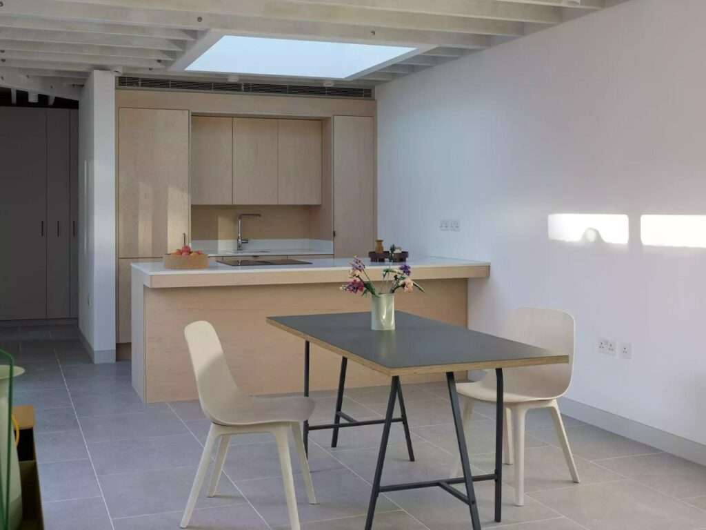 Minimalist dining table with chairs next to a kitchen island under natural light filtering down from above.