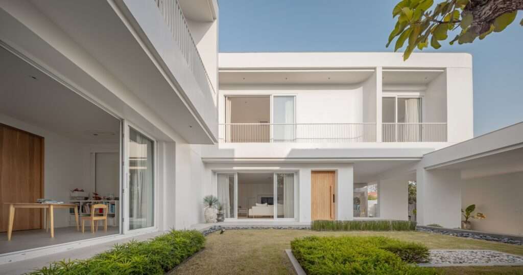 Wide shot of the L-shaped inner lawn at JNG House, highlighting large sliding glass doors that merge indoor spaces with the landscaped garden.