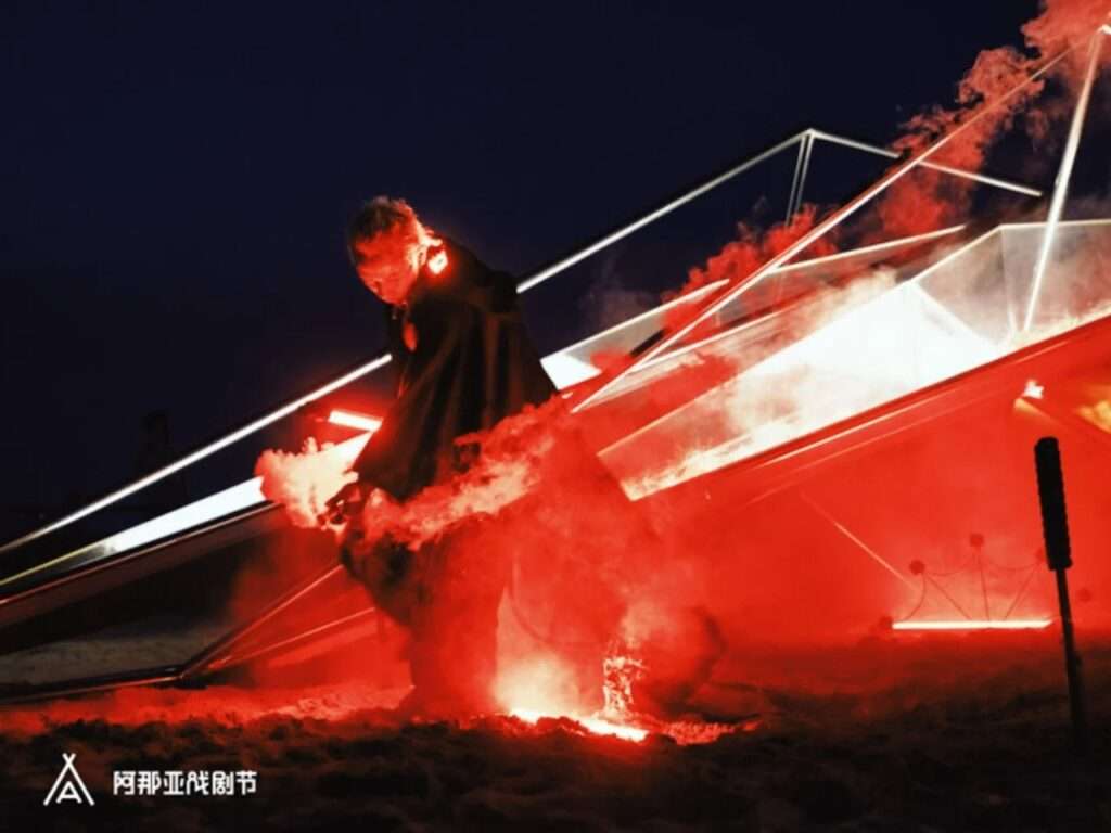 A performer surrounded by dense red smoke and bright red lighting next to the metal pavilion structure at night.