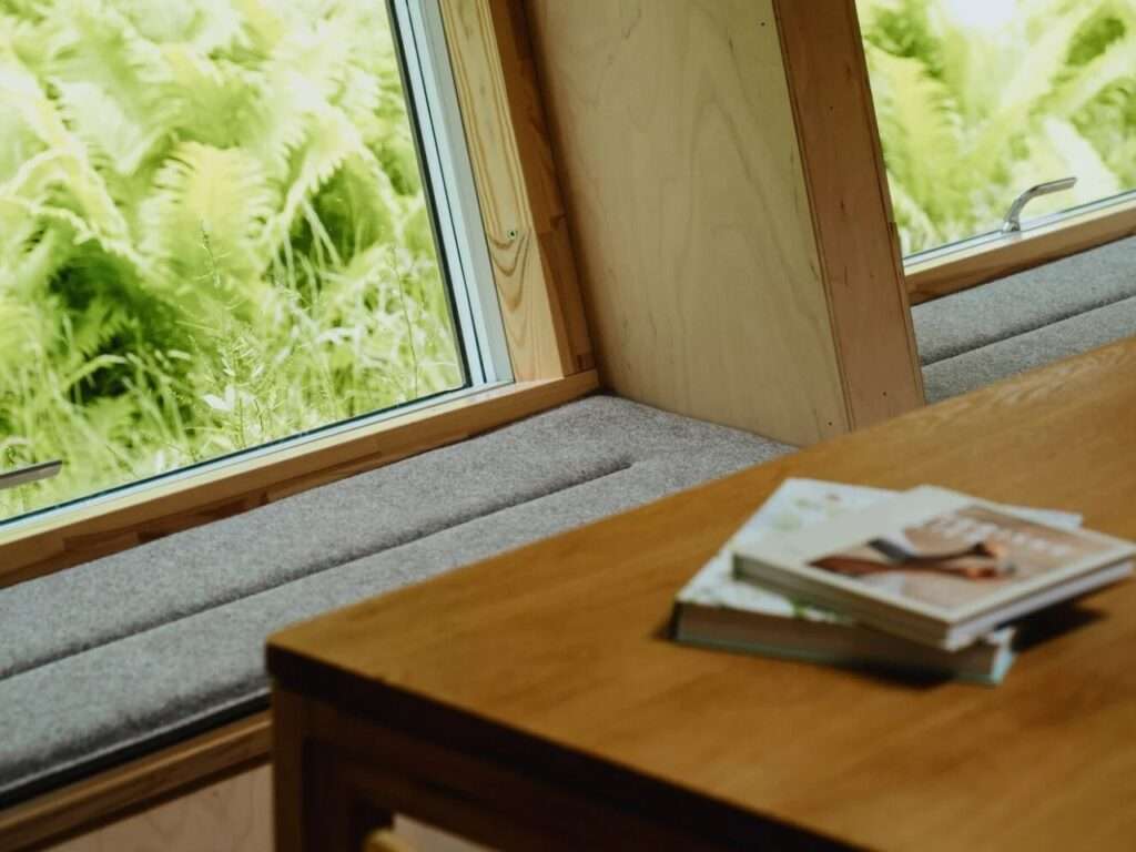 Built in window seating with gray upholstery next to a wooden dining table inside EcoNeo cabin.
