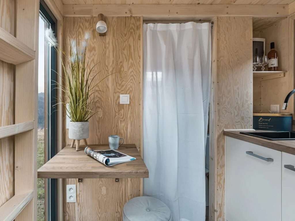 A wall-mounted foldable wooden table inside a tiny home next to a kitchen sink and a white curtain partition.