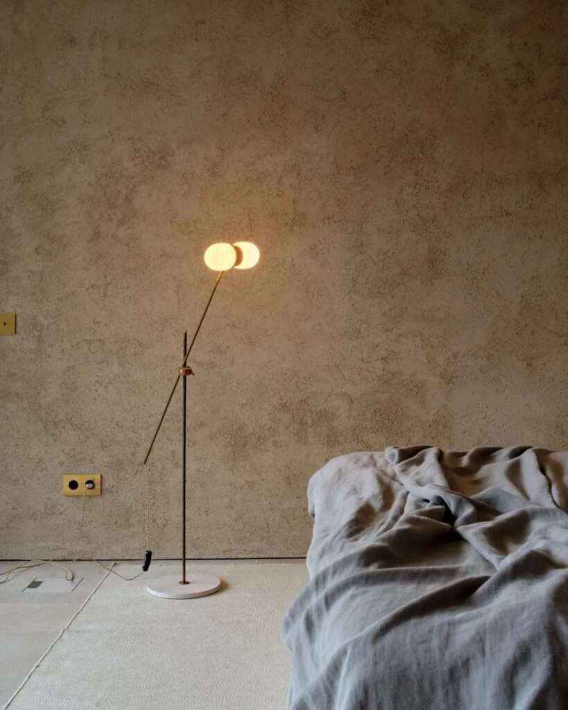 Minimalist interior view of a room with textured lime mortar walls, featuring a modern illuminated globe floor lamp and a low stone base.