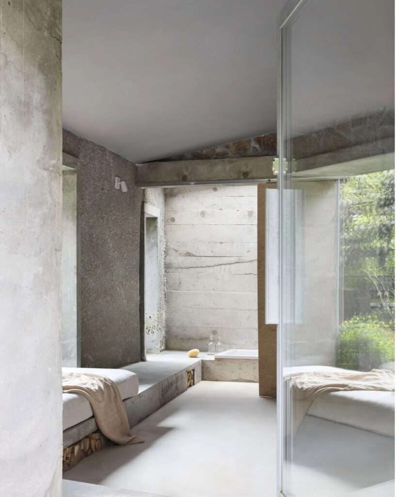Interior vista from the main room toward the sunken concrete bathtub and skylight through a large glass partition.