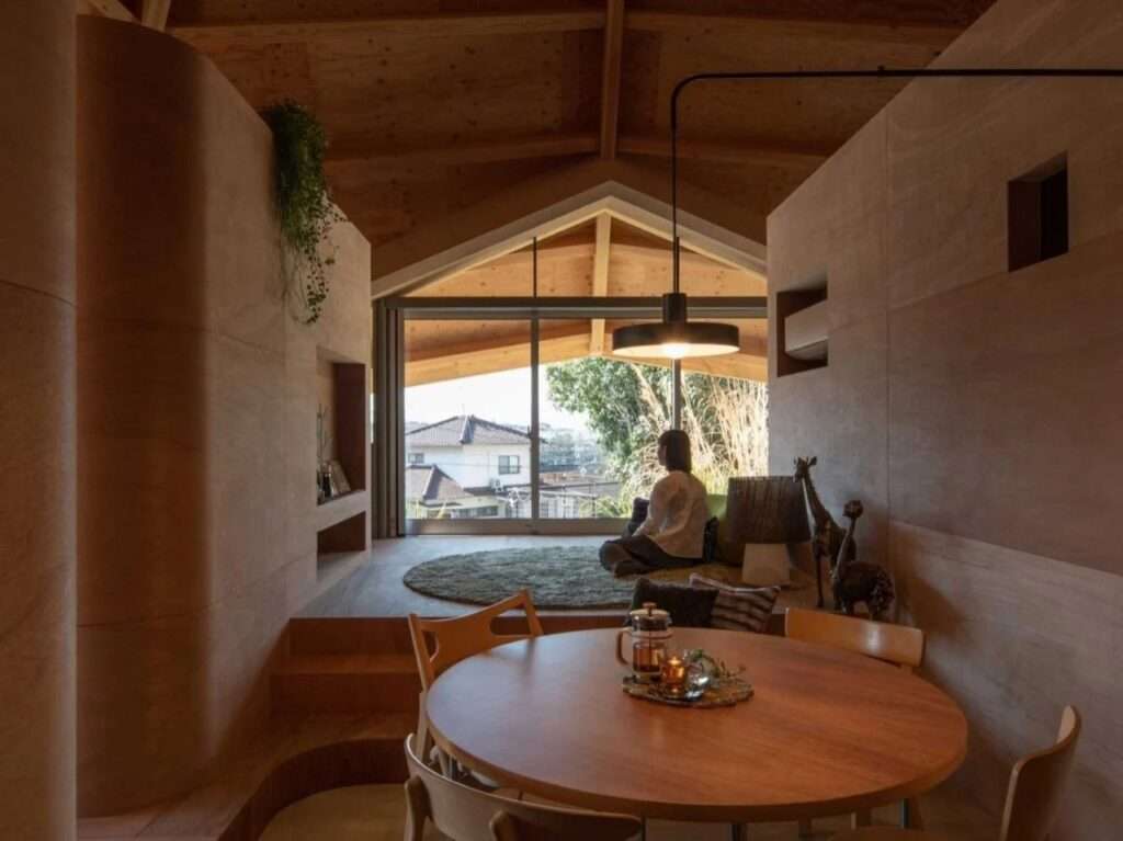 Cozy interior scene showcasing a dining table in the foreground and a resident sitting near a large glass sliding door looking out onto a residential neighborhood.