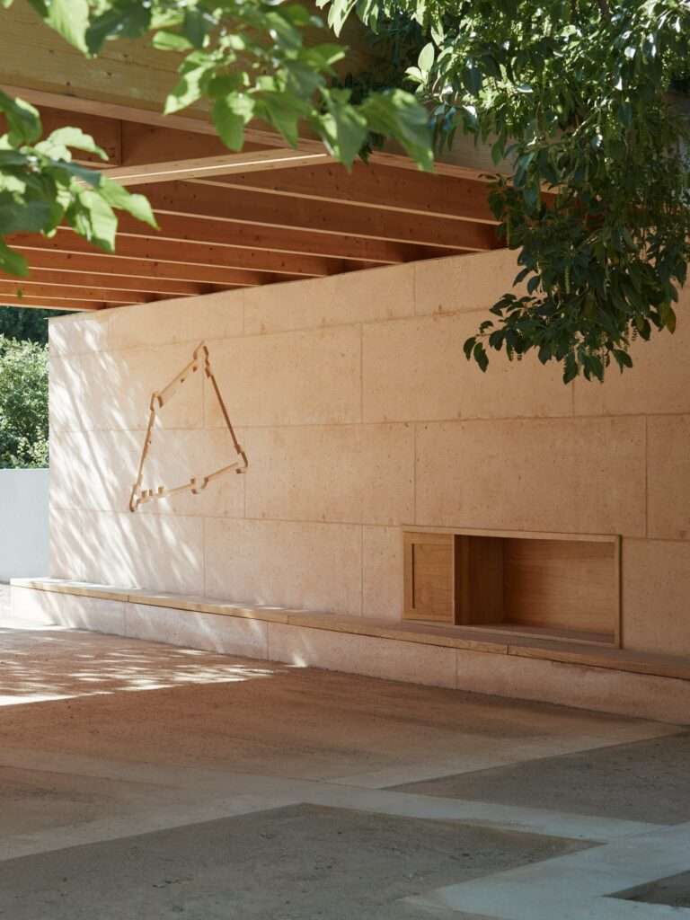 Linear perspective of a concrete wall featuring historical rampart engravings under cast shadows from an overhead wooden roof.