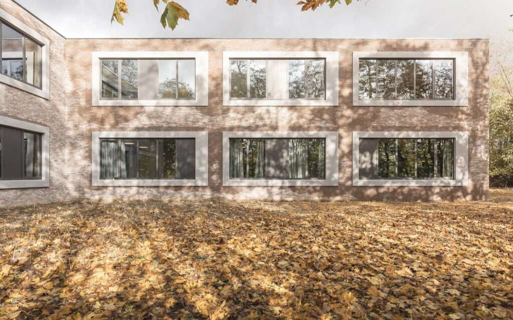 Red textured brick exterior wall of Cardinal Mercier College featuring large, deep-set rectangular framed windows reflecting trees.