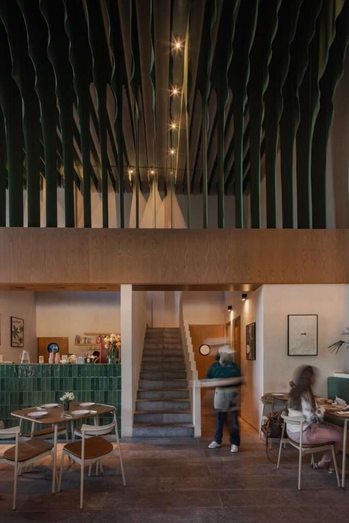 View facing the staircase leading to the mezzanine level with green ceiling fabric panels suspended directly above dining tables.