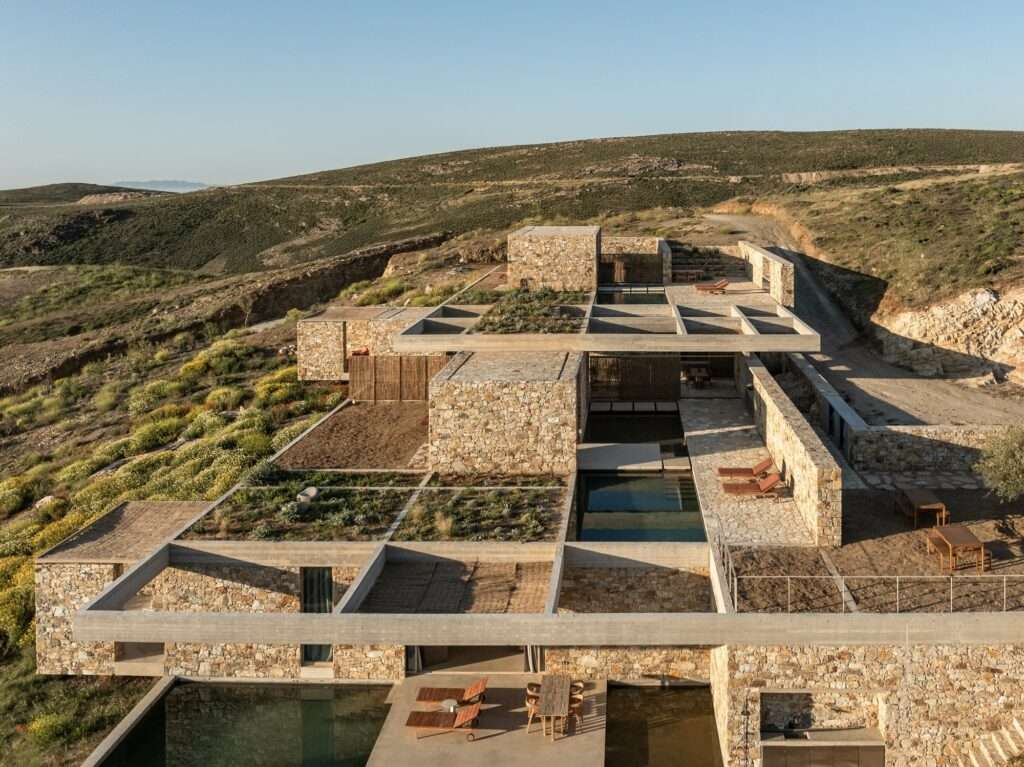 High-angle view of the Perma project, showcasing the geometric concrete grid and green roof gardens on the slopes of Serifos.