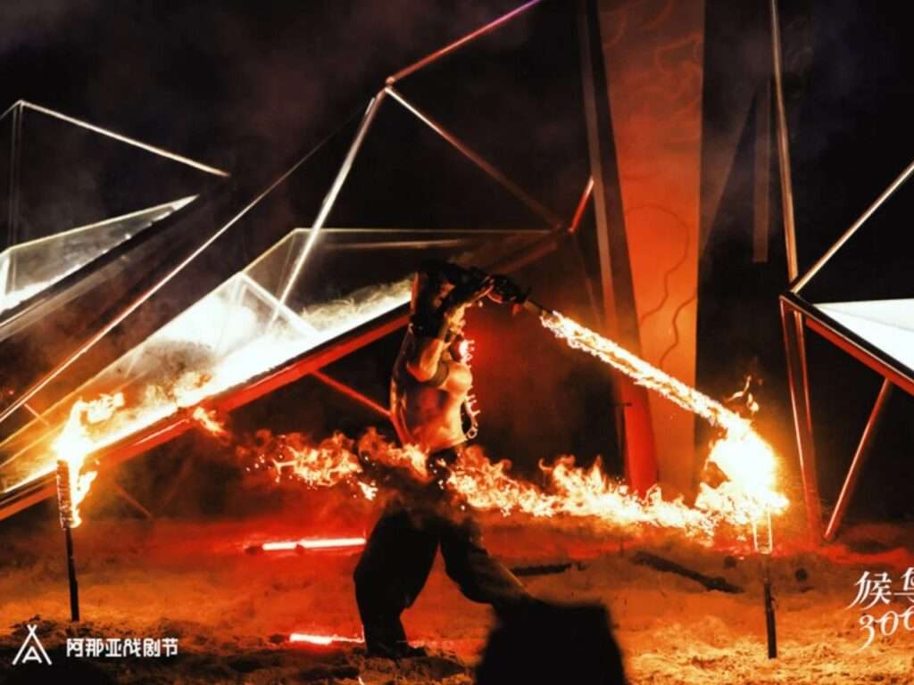 A performer wielding a flaming sword in front of the illuminated pavilion structure at night.