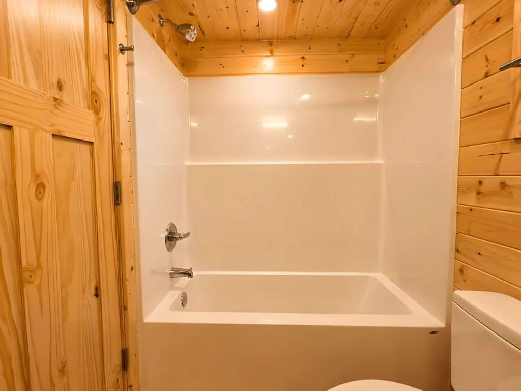 Compact bathroom interior within a tiny house showing a white integrated bathtub and shower combination next to a wooden privacy door.
