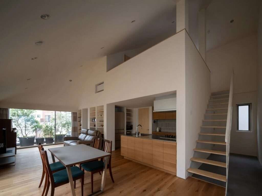 Open-plan dining and kitchen interior with sloped ceilings, timber stairs, and a mezzanine loft above.