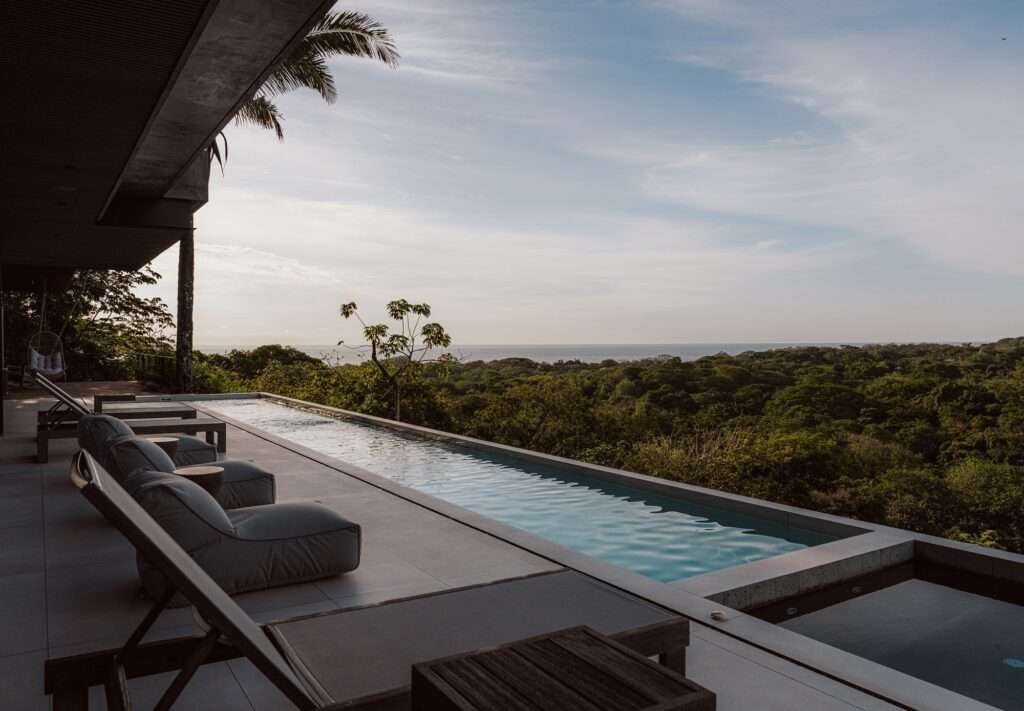 Long infinity pool on a shaded modern terrace overlooking a lush forest canopy at dusk at KUL Nosara.