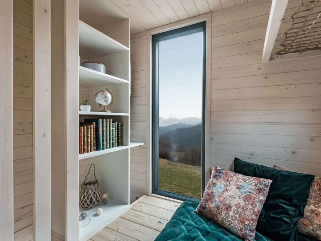 Cozy loft bedroom in La Ruche featuring custom white book shelving, velvet cushions, and a tall narrow view window.