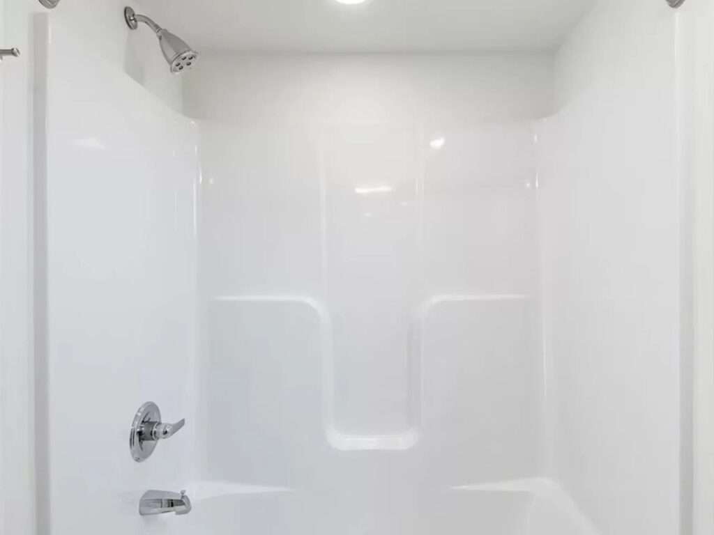 Clean, white modular shower unit in the N2 House bathroom, showing the silver showerhead and faucet hardware.