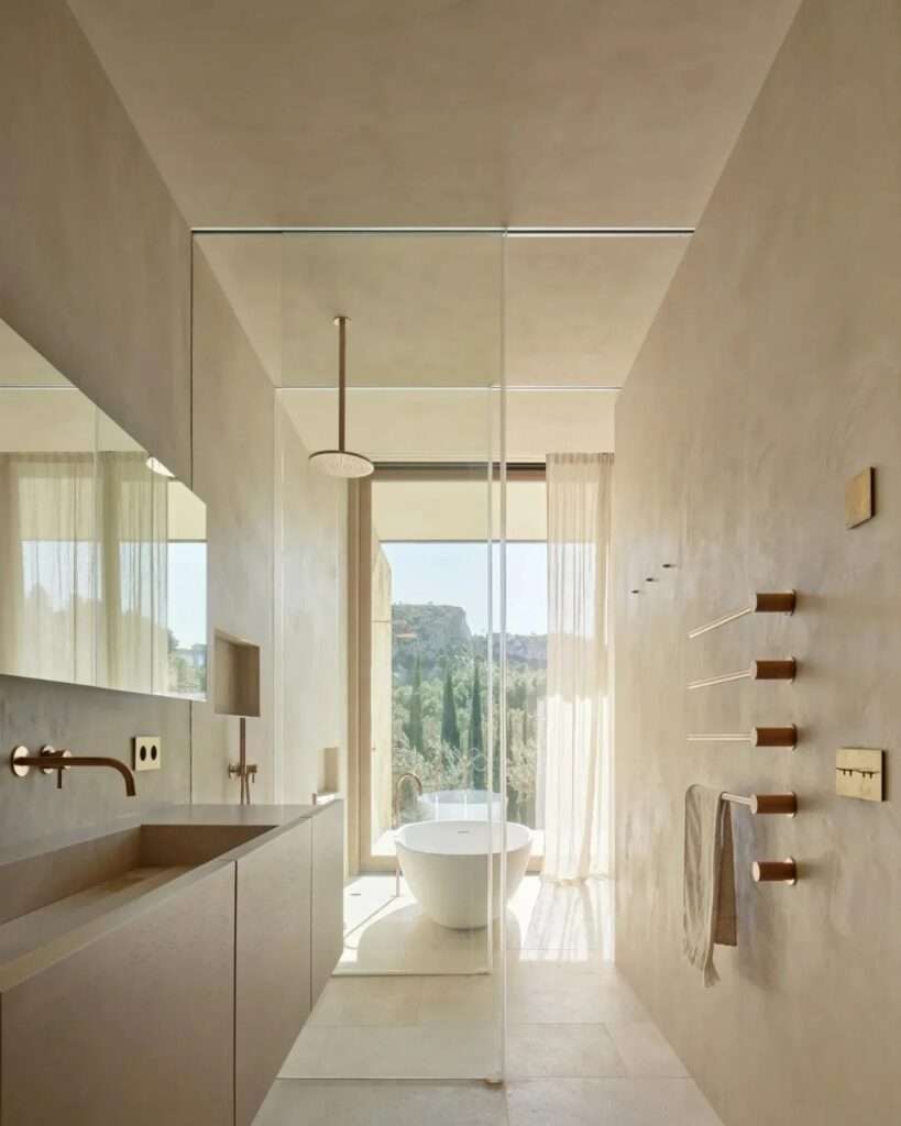 Interior view of a master bathroom in Casa Óculo, featuring custom wood cabinetry, copper fixtures, and a glass-enclosed shower framing a mountain view.