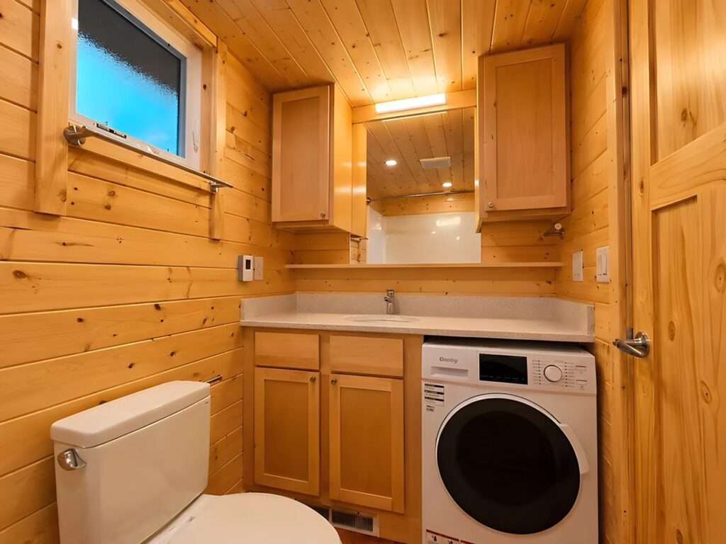 Tiny home bathroom vanity with a stone countertop, wooden under-sink cabinets, a large mirror, and an integrated white front-loading washer-dryer combo unit.