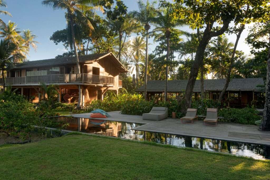 Wide view of the architectural complex showing the swimming pool, wooden deck, two-story house, and adjacent garden pavilion.