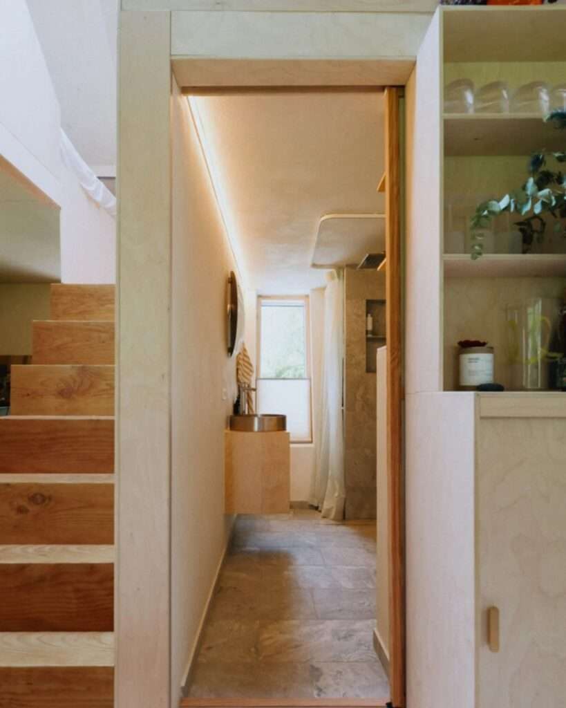 Narrow hallway corridor in EcoNeo cabin with timber stairs on the left and a compact bathroom sink straight ahead.