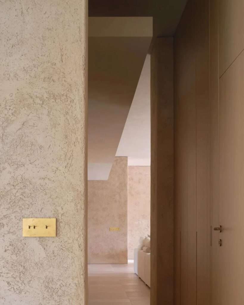 A view down a textured lime mortar hallway in Casa Óculo, showing the contrast between raw textured walls and warm wood cabinetry.