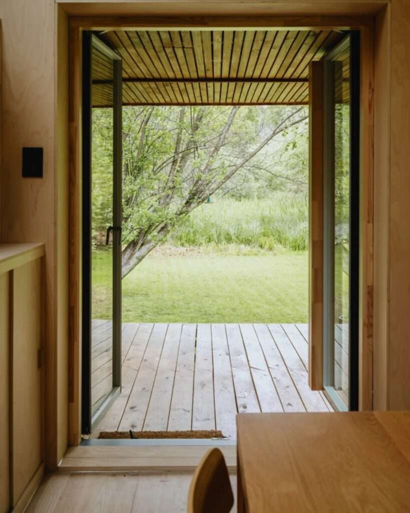 Open glass French doors of EcoNeo tiny home looking out to a green grass backyard lawn.