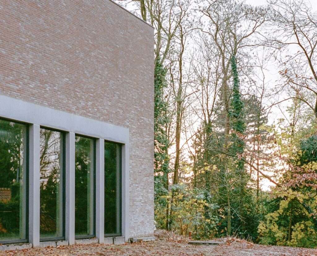 Corner detail of Cardinal Mercier College showcasing textured brickwork and minimalist floor-to-ceiling glass windows next to a forest.