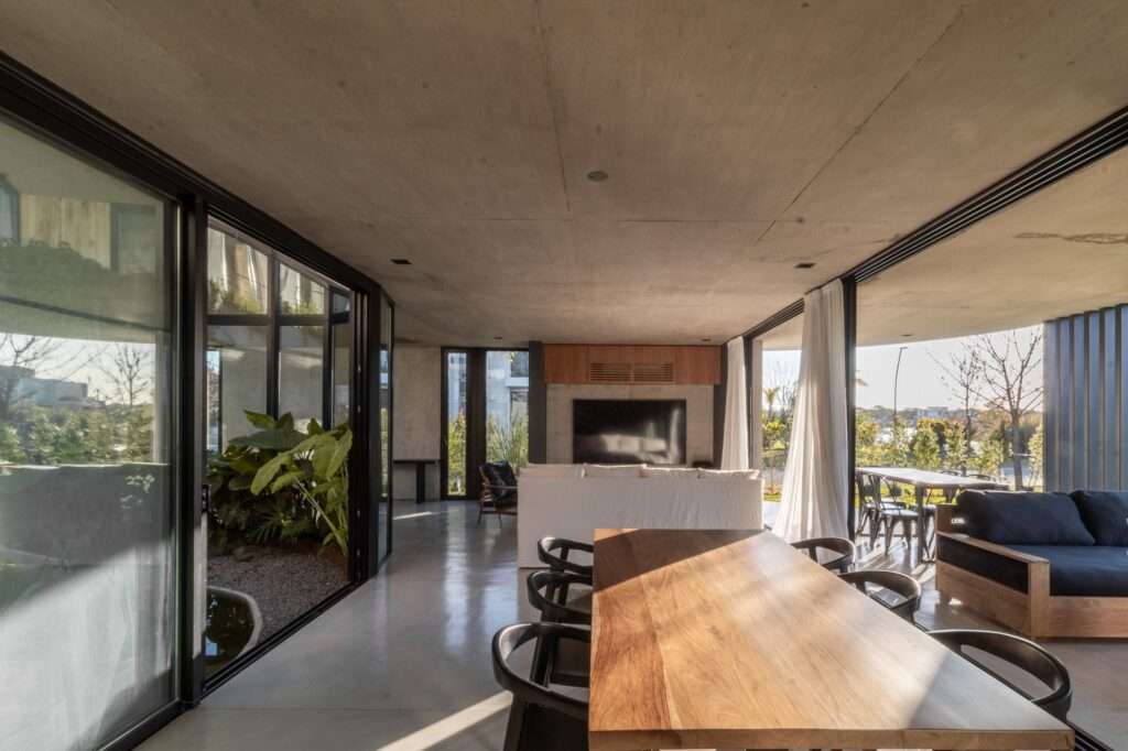 A spacious modern living and dining room with concrete floors, featuring wide sliding glass doors that open directly onto a central courtyard garden.