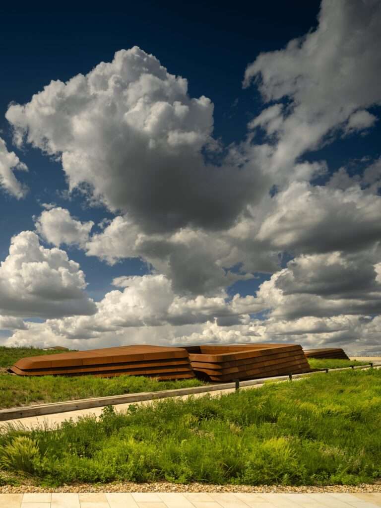A view of the library's green roof terrace featuring layered, rust-colored tectonic elements under a blue sky with clouds.