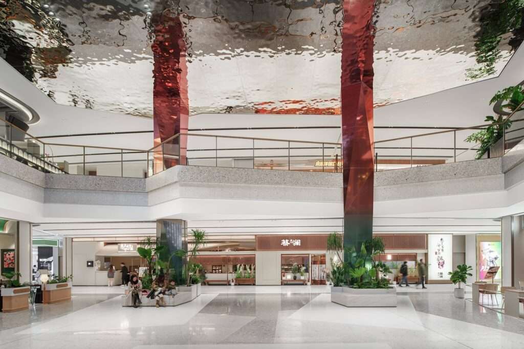 Indoor plaza at Wuxi MixC Mall with multi-faceted columns wrapped in copper mirrors, indoor plants, and a highly reflective rippled steel ceiling.