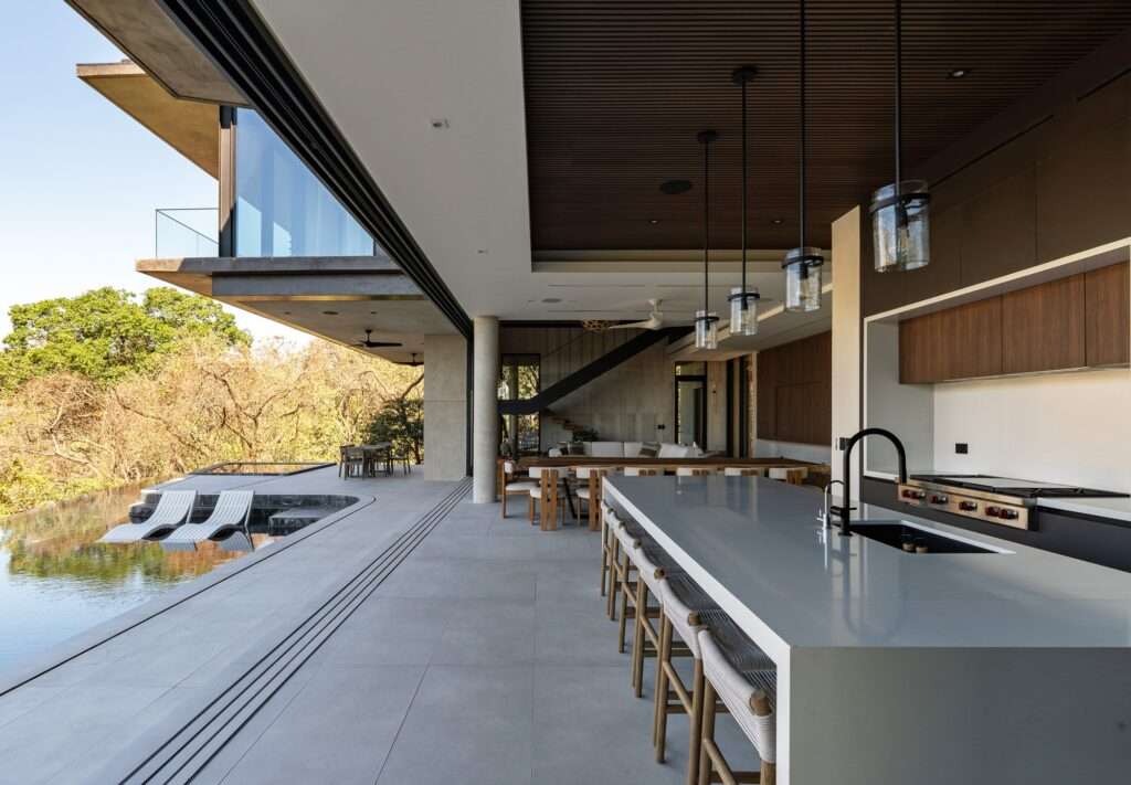 Open-concept luxury kitchen and dining area connected to an outdoor pool terrace with sliding glass walls at KUL Nosara.