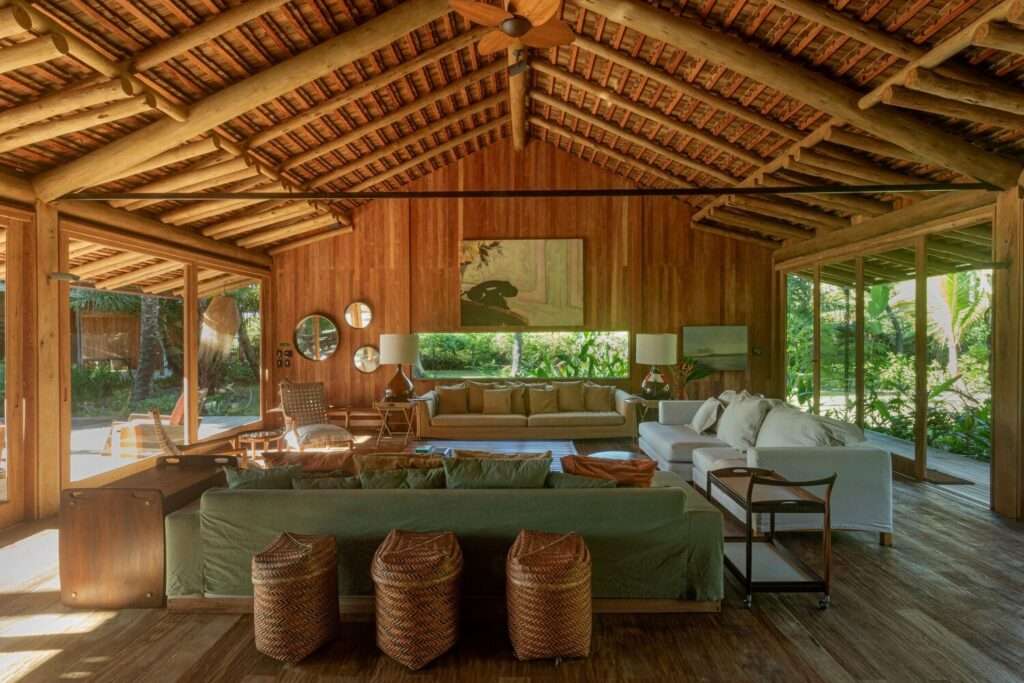 Cozy living room interior with green sofa, wicker ottomans, and large open windows framing garden views.