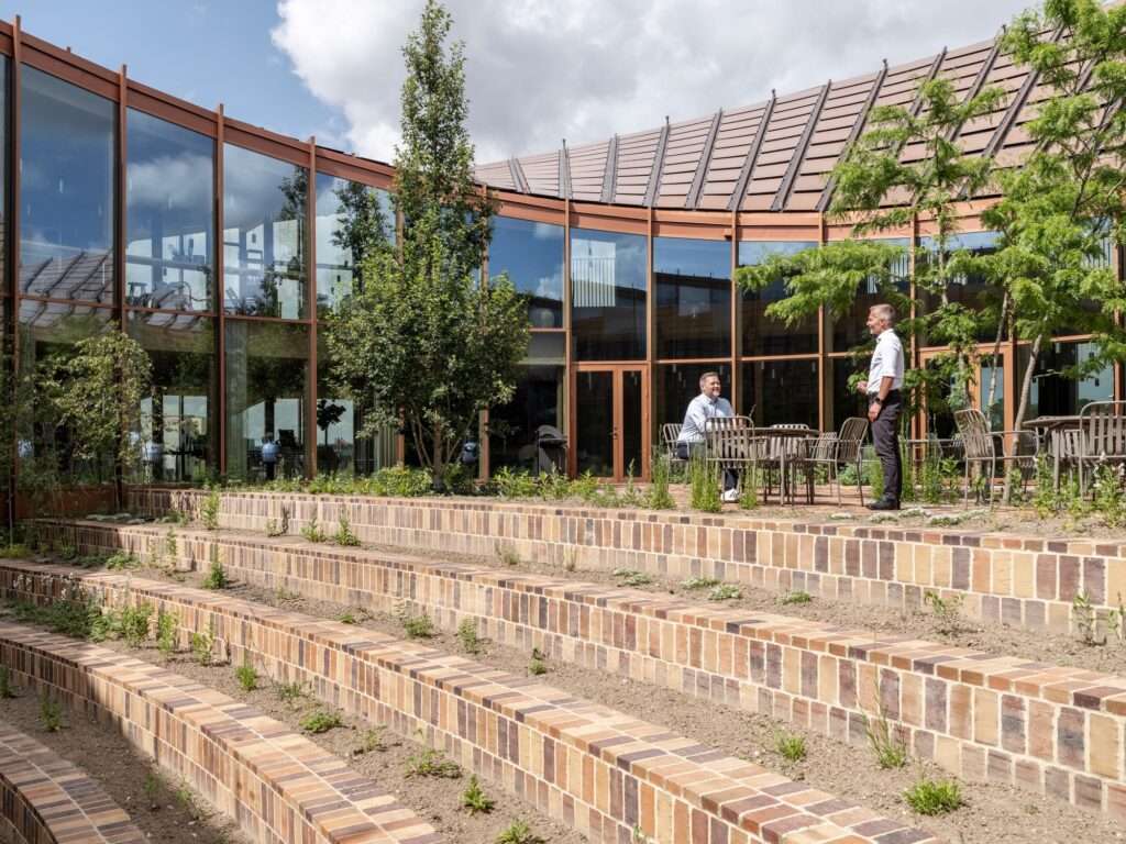 Two people conversing on an outdoor terrace within the terraced brick courtyard of Dymak HQ.