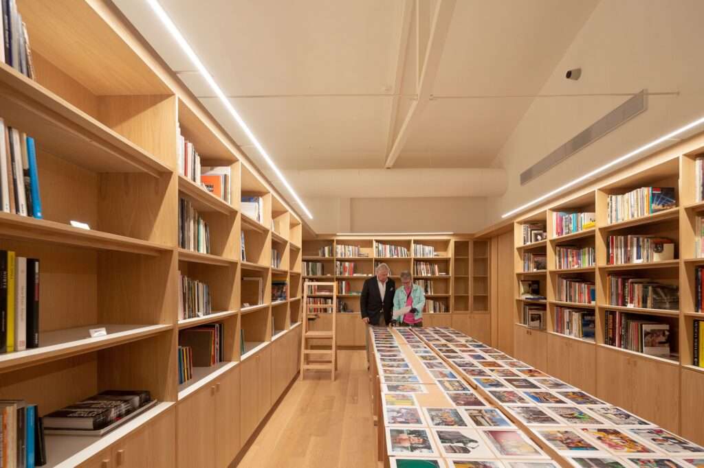 Interior of the specialist library at Larivière Foundation with floor-to-ceiling wooden bookshelves, a central table displaying photography books, and two visitors reviewing materials.