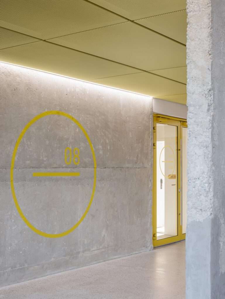 Raw concrete interior wall with a painted yellow circular graphic reading level 08 next to a yellow-framed glass door.
