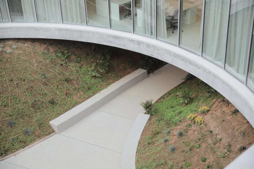 Top-down perspective of a concrete walking path curving through landscaped garden slopes beneath the circular office floor slab.