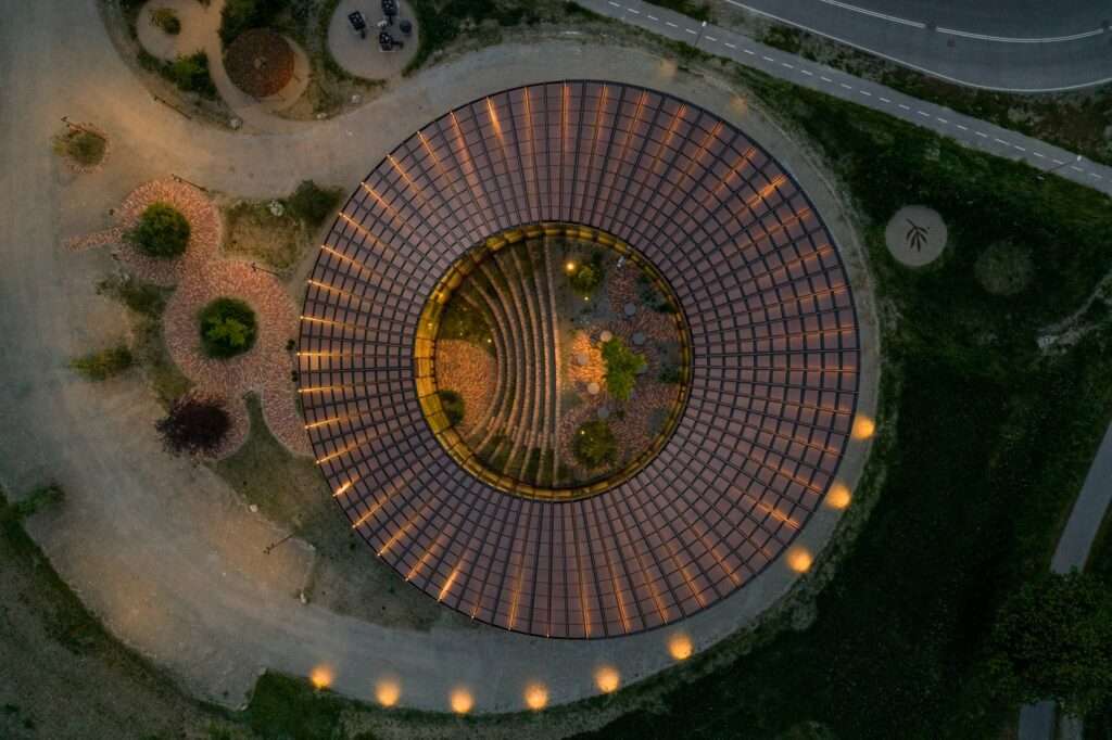 Direct top-down aerial view of the perfectly circular Dymak HQ building and its inner courtyard lit up at night.