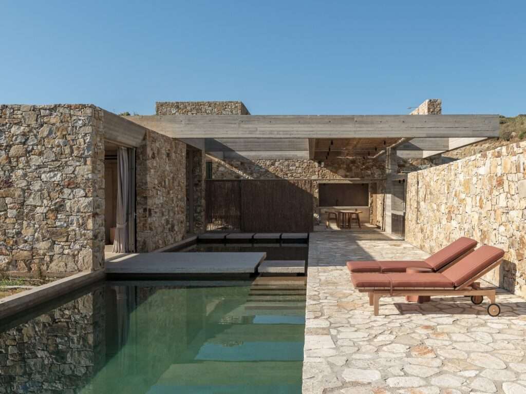 Outdoor lounge area with wooden sunbeds, stone terrace, and a tranquil water feature at the Perma project.