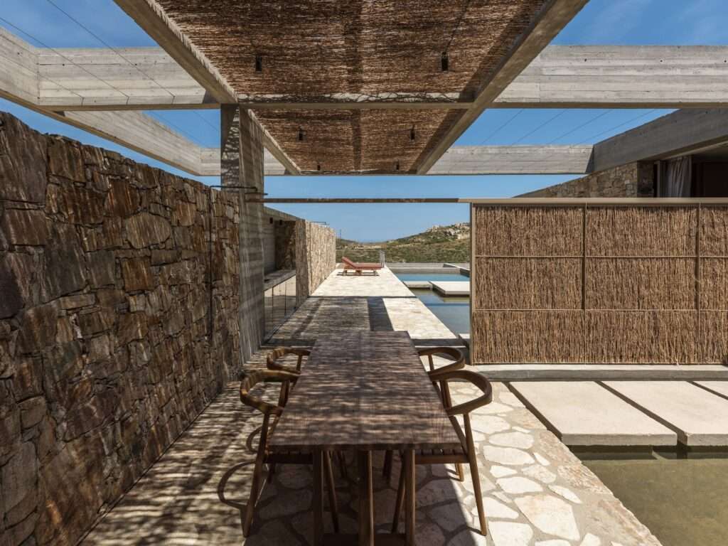 Shaded outdoor dining area with a reed canopy and stone walls in the Perma project.