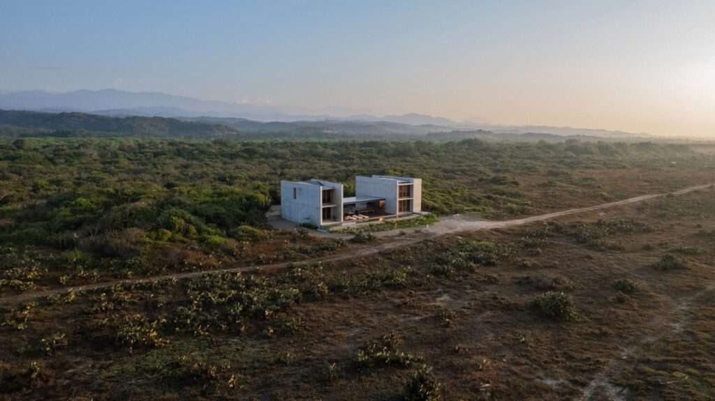 High aerial drone view of Casa Macahuite surrounded by dense green vegetation and desert flora in a coastal setting.