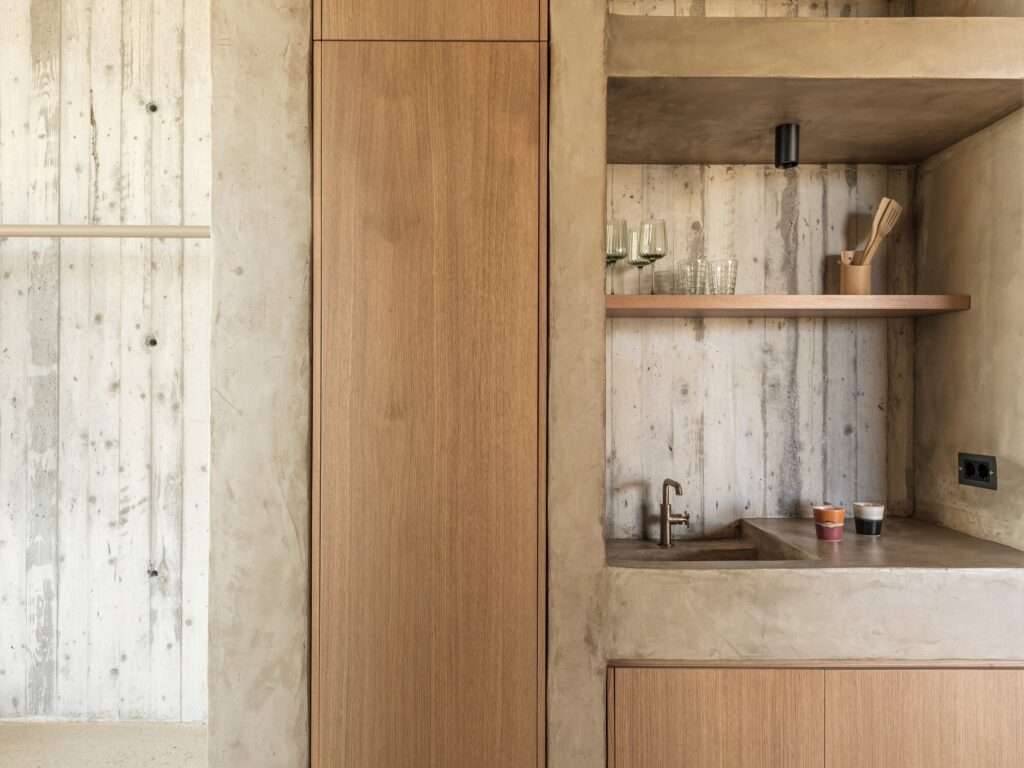 Minimalist kitchen area featuring exposed concrete walls and wooden joinery in the Perma residence.