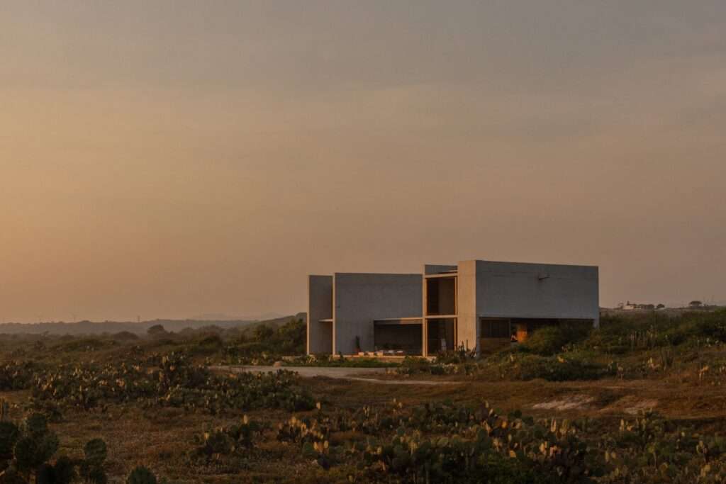 Exterior side view of Casa Macahuite during sunset, showing solid concrete walls and warm interior lighting.
