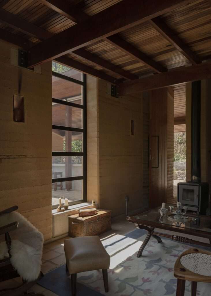 A warm, sunlit interior view looking out from the living area towards the covered outdoor kitchen, framed by large glass panels.