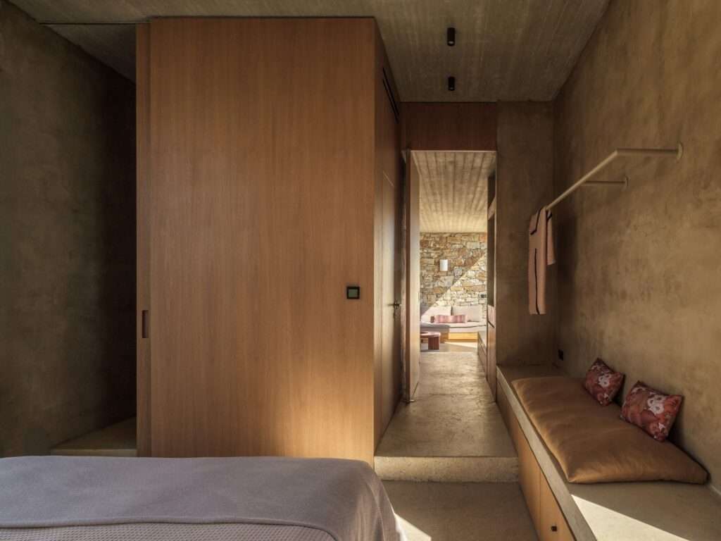 Interior bedroom hallway with stone walls, wooden partition, and a view into the living area of the Perma house.