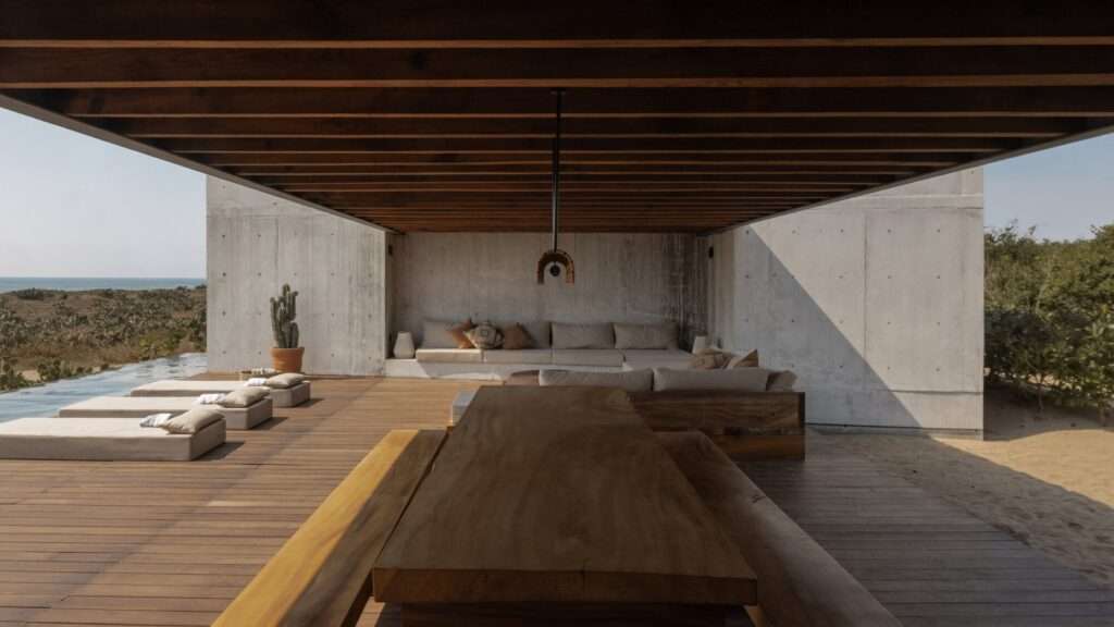 Long wooden dining table and built-in concrete lounge sofa under a exposed timber beam ceiling structure.