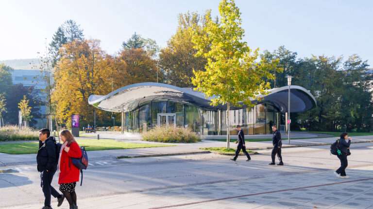 Glazed circular pavilion with an undulating mirrored roof surrounded by trees and pedestrians