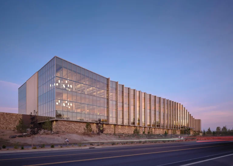 Exterior view of a modern library building with angled glass facade and stone base at dusk.